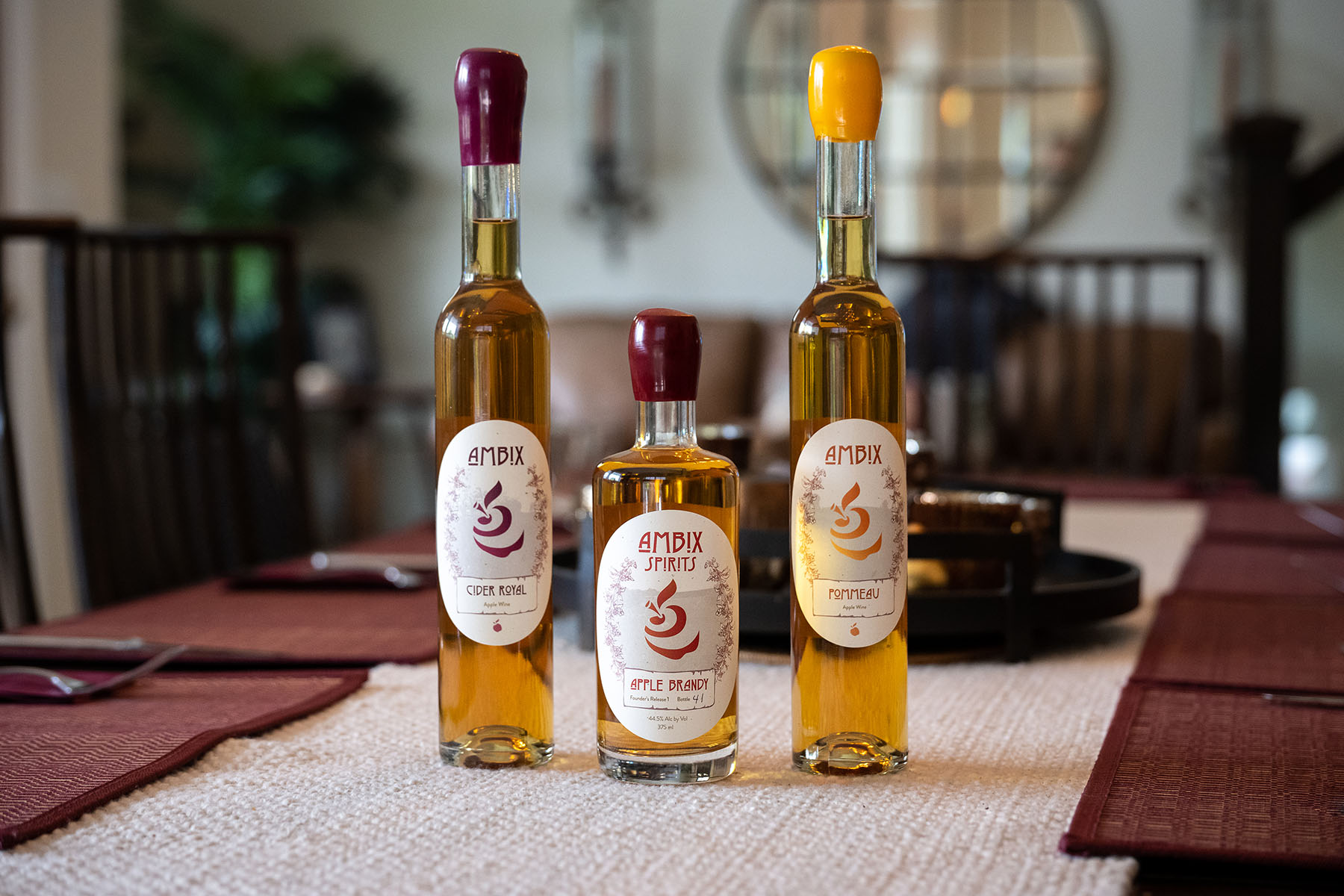 Three Ambix Spirits products: Pommeau, Apple Brandy, and Cider Royal, being showcased on a dining table.